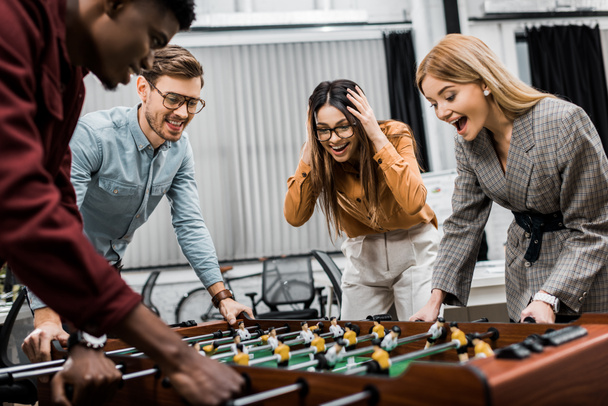 emotional multicultural business colleagues playing table football together in office - Foto, Imagem