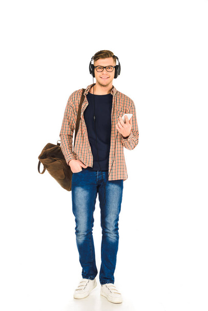handsome man standing in headphones and holding  smartphone isolated on white - Foto, afbeelding