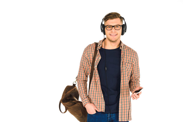 pohledný muž, poslech hudby ve sluchátkách a držení smartphone izolované na bílém - Fotografie, Obrázek
