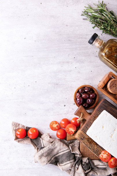 Traditional greek appetizer goat feta cheese served with fresh cherry tomatoes, herbs, green and black olives and extra virgin olive oil over a grey background. Top view. Copy space - 写真・画像