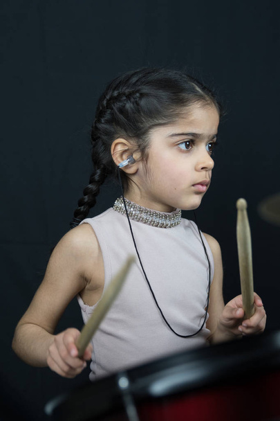 5 year old girl of British Indian origin practicing and playing the drums, reading music from notation - on a dark background with copy space.  - Photo, Image