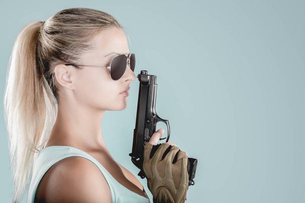 Sexy girl wearing military style posing with guns and sunglases isolated in studio - Fotó, kép
