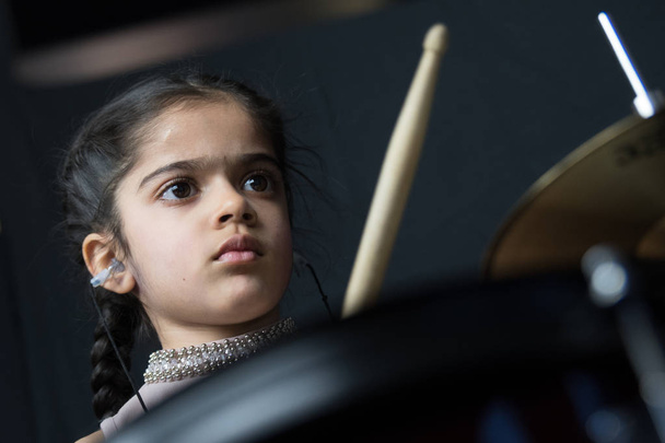 5 year old girl of British Indian origin practicing and playing the drums, reading music from notation - on a dark background with copy space.  - 写真・画像