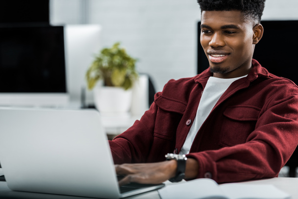 portrait of smiling african american businessman working on laptop in office - Zdjęcie, obraz