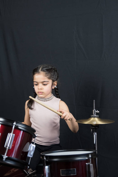 5-letnia dziewczyna z brytyjskiego pochodzenia indyjskiego, ćwiczenia i gry na perkusji, czytania muzyki z notacji - na ciemnym tle z miejsca kopii.  - Zdjęcie, obraz