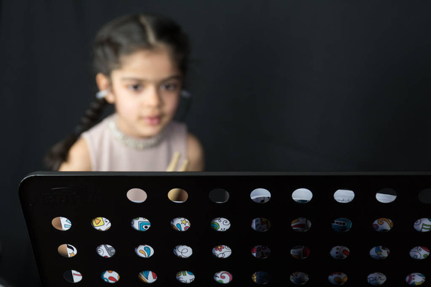 Una niña de 5 años de etnia india británica - practicando en la batería y leyendo notas musicales - sobre un fondo negro oscuro
. - Foto, Imagen