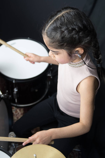 Uma menina de 5 anos de idade de etnia indiana britânica - praticando na bateria e lendo notas musicais - em um fundo preto escuro
. - Foto, Imagem