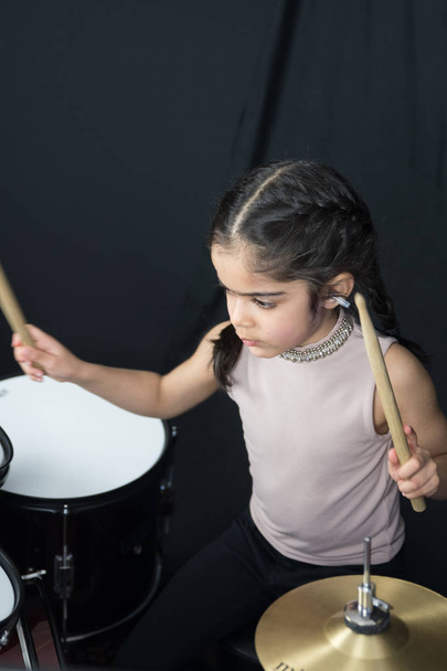 5-letnia dziewczyna z British Indian etniczna - ćwiczenia na perkusji i czytanie nut - na ciemnym tle czarny. - Zdjęcie, obraz