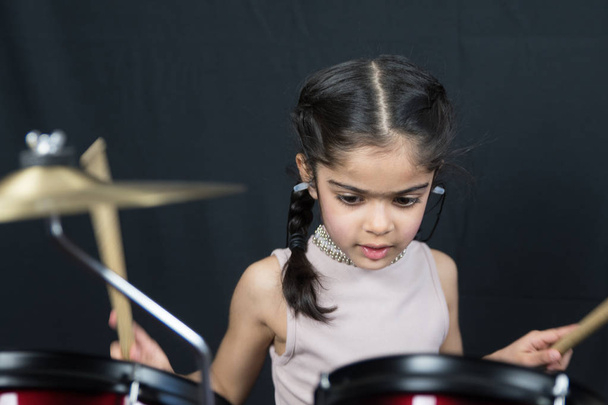 Uma menina de 5 anos de idade de etnia indiana britânica - praticando na bateria e lendo notas musicais - em um fundo preto escuro
. - Foto, Imagem