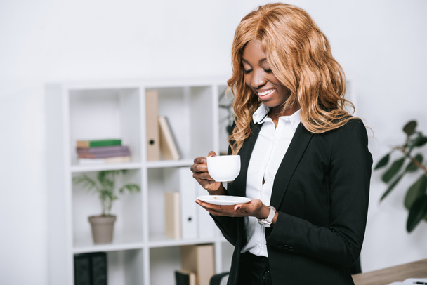 Gelukkig Afro-Amerikaanse zakenvrouw kopje koffie houden in moderne kantoren  - Foto, afbeelding