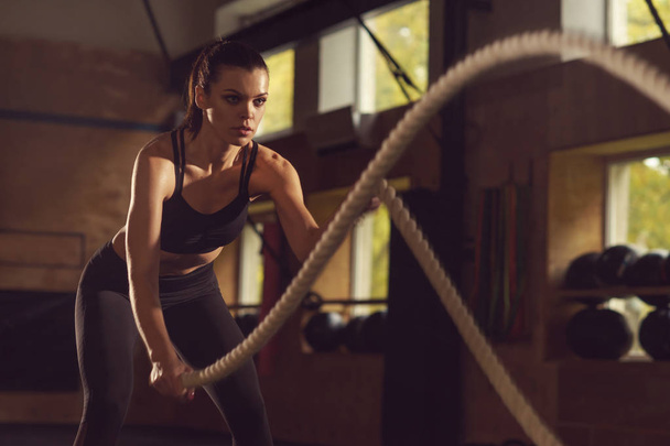 Fit, sporty and athletic sportswoman working in a gym. Womantraining using battle ropes. Sports, athletics, lifestyle and fitness concept. - Valokuva, kuva