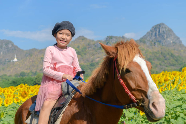 glückliches nettes Mädchen reitet Pferd in Sonnenblumenfeld am blauen Himmel, lop buri.thailand - Foto, Bild