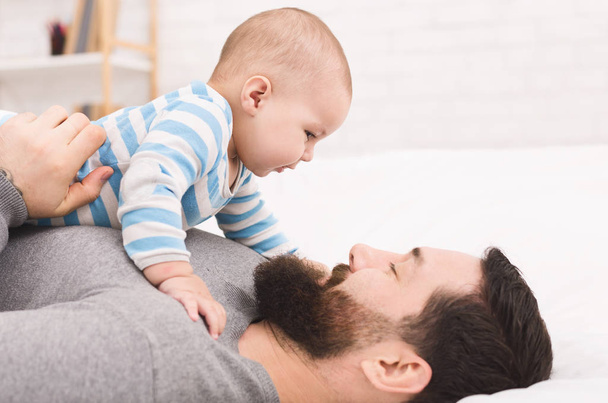 Vater-Sohn-Verbindung. entzückendes Baby, das in die Augen des Vaters schaut, auf seiner Brust liegend - Foto, Bild