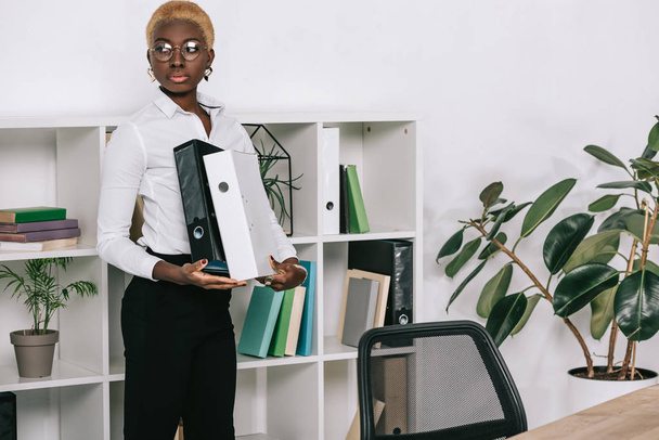красивая африканская американская бизнесвумен, держащая папки в современном офисе
 - Фото, изображение