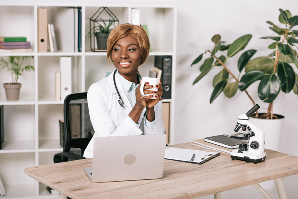 smiling female african american scientist holding cup with drink  - Foto, imagen