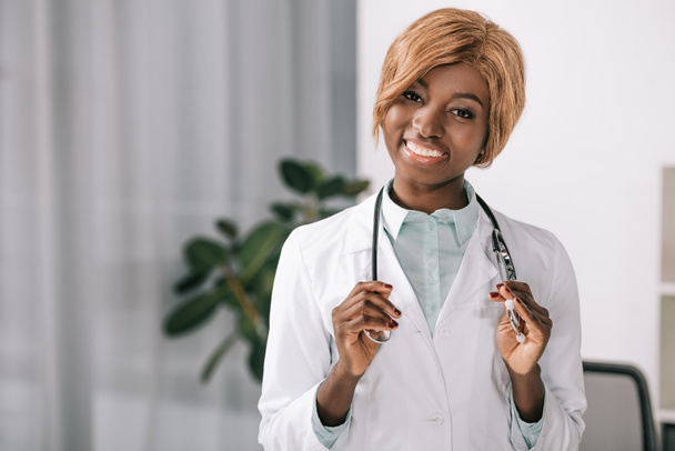 attraente sorridente donna africana americana che tiene lo stetoscopio mentre guarda la fotocamera
 - Foto, immagini