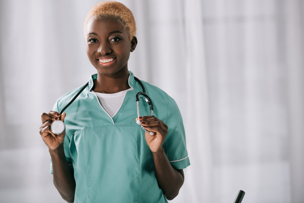 attractive cheerful african american woman holding stethoscope while looking at camera - Photo, Image