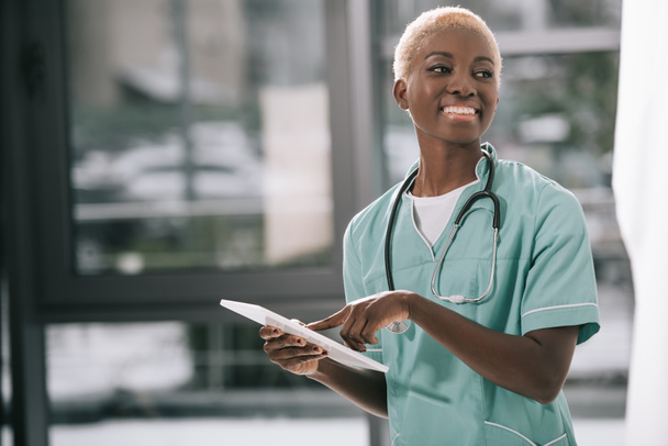 femme afro-américaine souriante avec stéthoscope en utilisant une tablette numérique en clinique
 - Photo, image