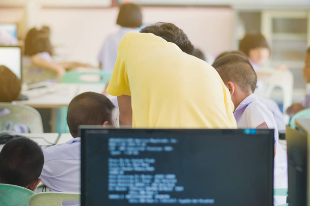 männlicher Lehrer in gelbem Hemd geht durch die Klasse, hilft und überprüft Arbeiten von Schülern im Computerunterricht. - Foto, Bild