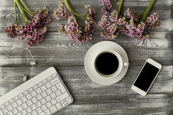 Top view of a keyboard, headphones and a cup of coffee, phone and a purple flower on a gray wooden table. Flat design - 写真・画像