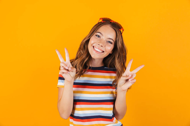 Portrait of a smiling cheerful young girl standing isolated over yellow background, wearing funny sunglasses, posing - Фото, зображення