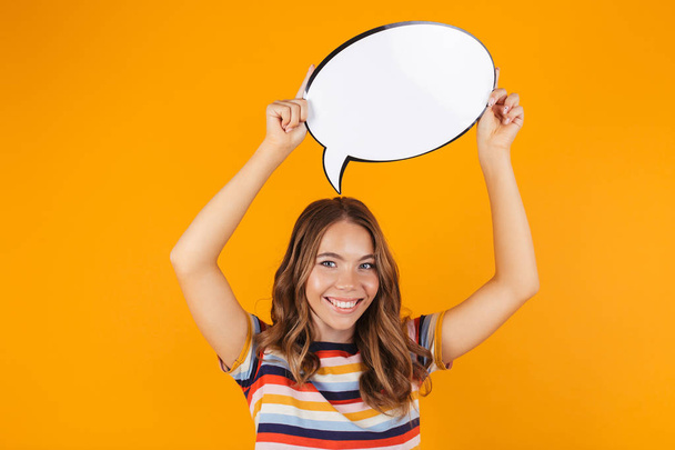 Image of happy young beautiful girl posing isolated over yellow background holding speech bubble. - Foto, Bild