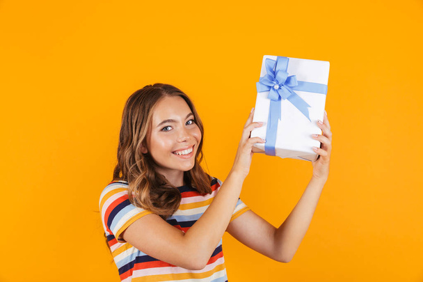 Image of cute young beautiful girl posing isolated over yellow background holding gift box. - Фото, изображение