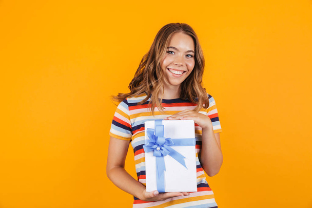 Image of cute young beautiful girl posing isolated over yellow background holding gift box. - Φωτογραφία, εικόνα