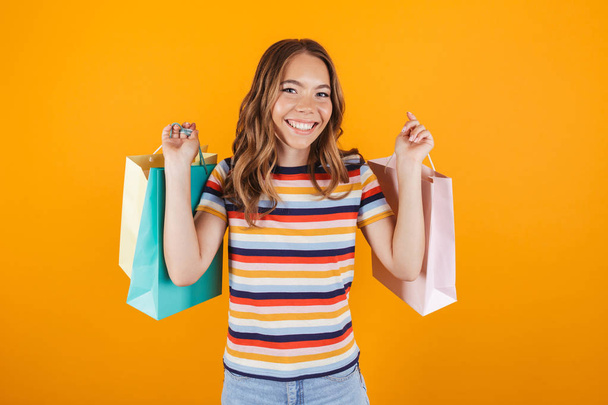Image of a happy young girl posing over yellow wall background holding shopping bags. - Фото, зображення