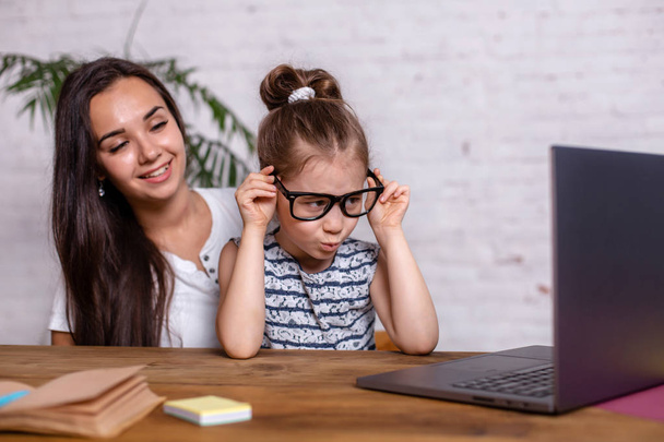Attractive young woman and her little cute daughter are sitting at the table and having fun while doing homework together. - Foto, immagini