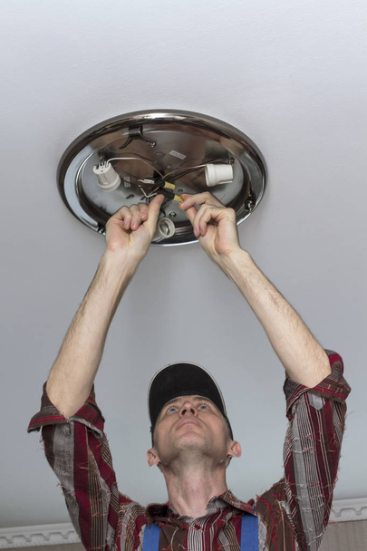 Електрик встановлює освітлювальну лампу на стелю приміщення
 - Фото, зображення