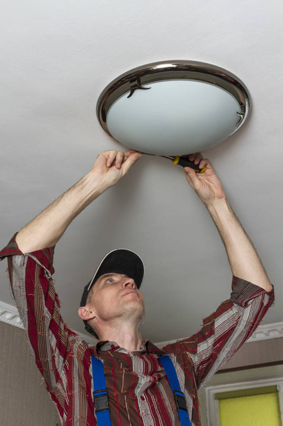 Electricista instalando lámpara de iluminación en el techo de la habitación
 - Foto, imagen