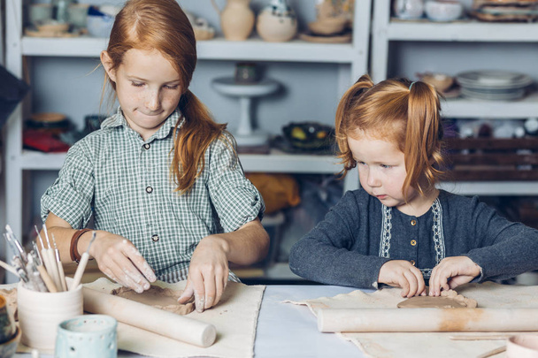 ginger elder sister teaching to her little sister to create a clay dishes - Фото, изображение
