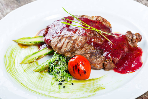 Grilled ribeye beef steak with berry sauce, asparagus and broccoli on light wooden background. Hot Meat Dishes. Top view, flat lay - Photo, Image