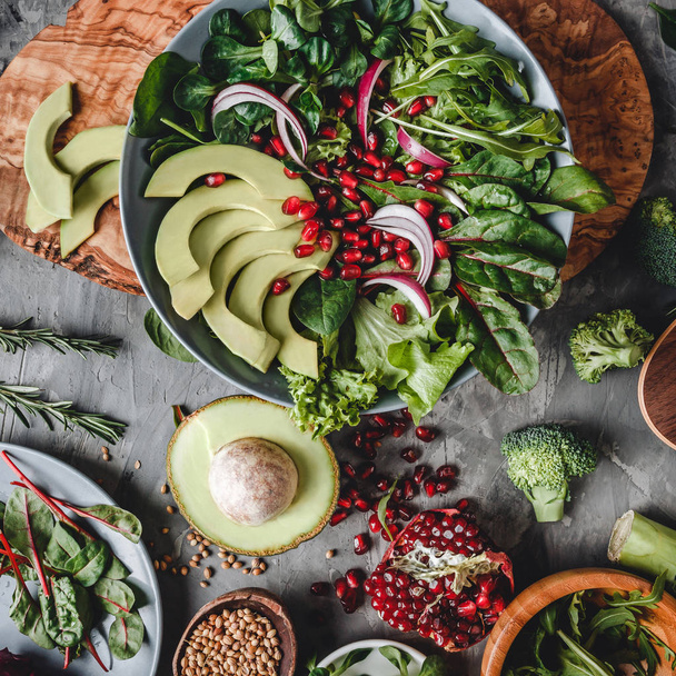 Healthy fresh salad with avocado, greens, arugula, spinach, pomegranate in plate over grey background. Healthy vegan food, clean eating, dieting, top view - Foto, imagen
