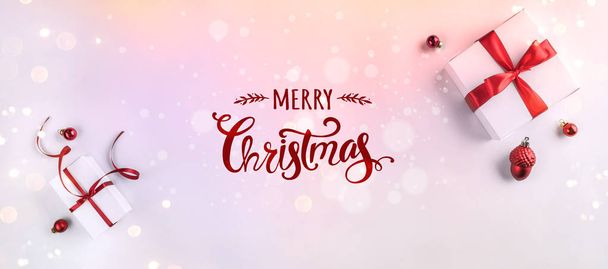 Merry Christmas Typographical on white background with gift boxes, fir branches, red decoration. Xmas and New Year card, bokeh, light. Flat lay, top view - Фото, изображение