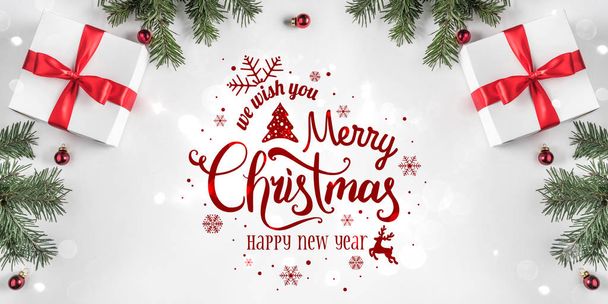 Merry Christmas Typographical on white background with gift boxes, fir branches, red decoration. Xmas and New Year card, bokeh, light. Flat lay, top view - Фото, изображение