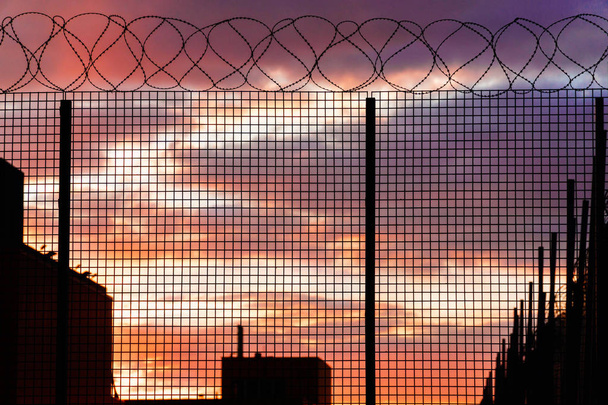 Contrast silhouette of barbed wire fence against a colorful cloudy sky. Sunset  - Photo, Image