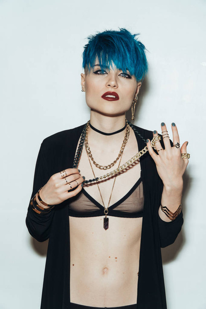 fashion photography of a girl with blue hair on a white background looking straight into the camera. Thick yellow chain and bijouterieher on her neck. Professional model posing in studio - Photo, Image