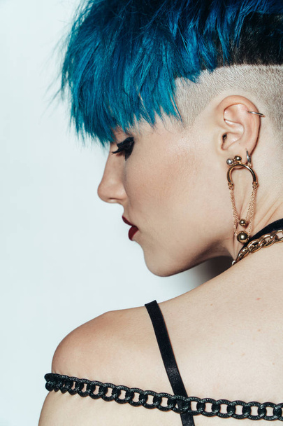 fashion photography of a girl with blue hair on a white background shot from the back. Thick yellow chain and bijouterieher on her neck. Professional model posing in studio - Φωτογραφία, εικόνα