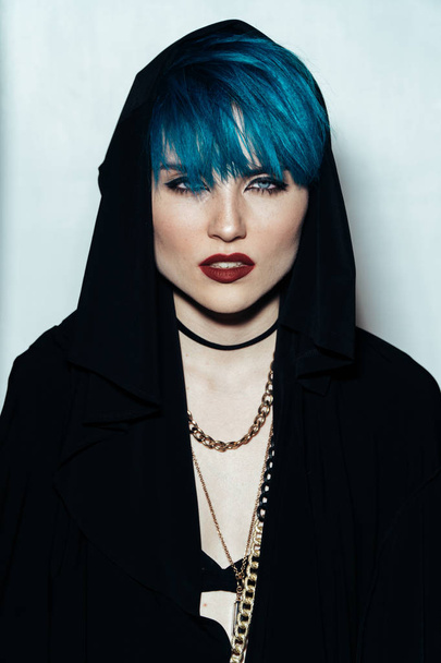 fashion photography of a girl with blue hair on a white background looking directly at the camera. Thick yellow chain and bijouterieher on her neck. Professional model posing in studio - Fotoğraf, Görsel