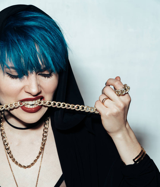 Close up fashion portrait photography of a girl with blue hair on a white background She bites a thick yellow chain. Professional model posing in studio. - Foto, Bild