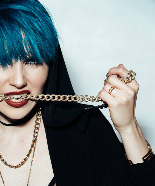 Close up fashion portrait photography of a girl with blue hair on a white background She bites a thick yellow chain. Professional model posing in studio. - Photo, Image