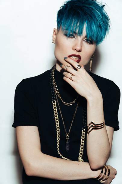 fashion photography of a girl with blue hair on a white background looking directly at the camera. Thick yellow chain and bijouterieher on her neck. Professional model posing in studio - Φωτογραφία, εικόνα