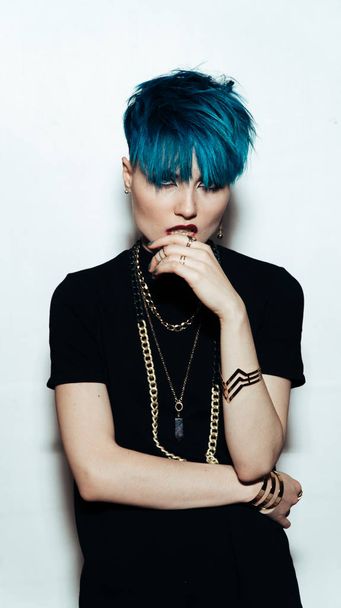 fashion photography of a girl with blue hair on a white background looking directly at the camera. Thick yellow chain and bijouterieher on her neck. Professional model posing in studio - Foto, afbeelding