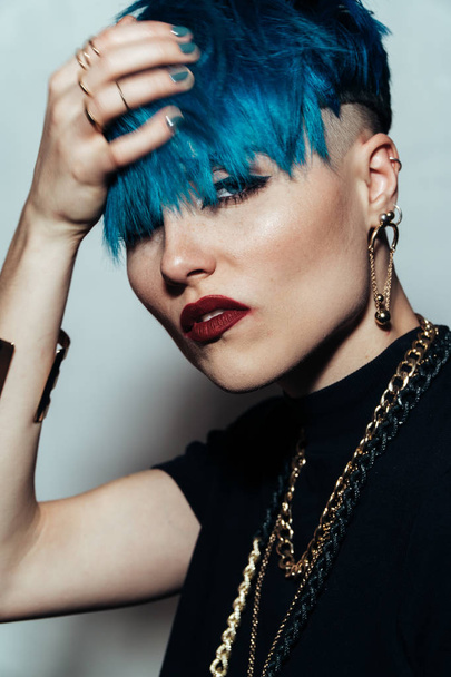 fashion photography of a girl with blue hair on a white background looking directly at the camera. Thick yellow chain and bijouterieher on her neck. Professional model posing in studio - Фото, изображение