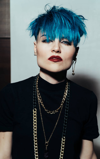 fashion photography of a girl with blue hair on a white background looking directly at the camera. Thick yellow chain and bijouterieher on her neck. Professional model posing in studio - Valokuva, kuva