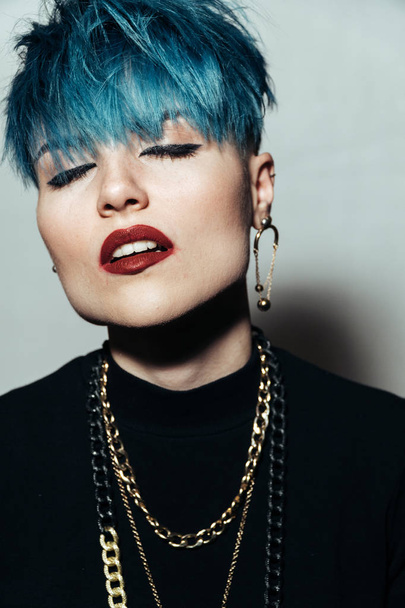 fashion photography of a girl with blue hair on a white background looking directly at the camera. Thick yellow chain and bijouterieher on her neck. Professional model posing in studio - Photo, Image