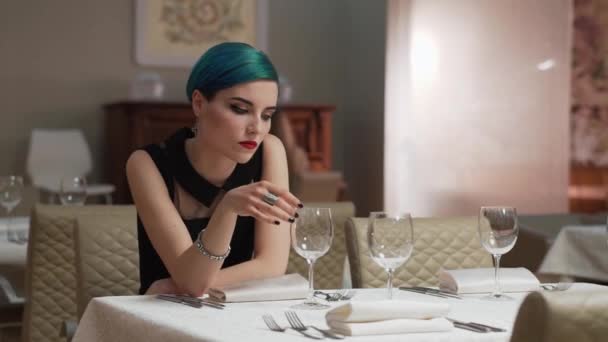 Mooie triest vrouw met kort blauw haar, alleen zittend in restaurant, wachten op iemand. Sad en depressie, lege glazen op tafel. Mislukte datum.  - Video