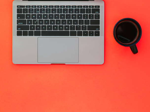 Černý hrnek s kávou a šedý notebook na červeném pozadí. Minimalismus plošné uspořádání pracoviště - Fotografie, Obrázek